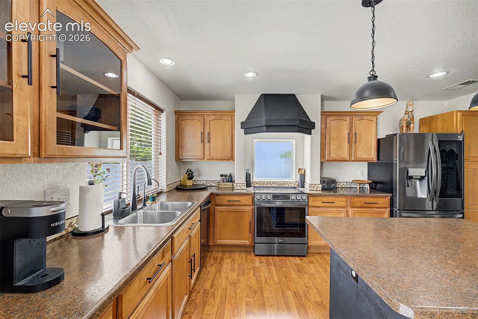 Generous counter space wraps the perimeter of this functional kitchen, with a deep double sink beneath a window, a slide-in range, and a dramatic black range hood as the focal centerpiece.