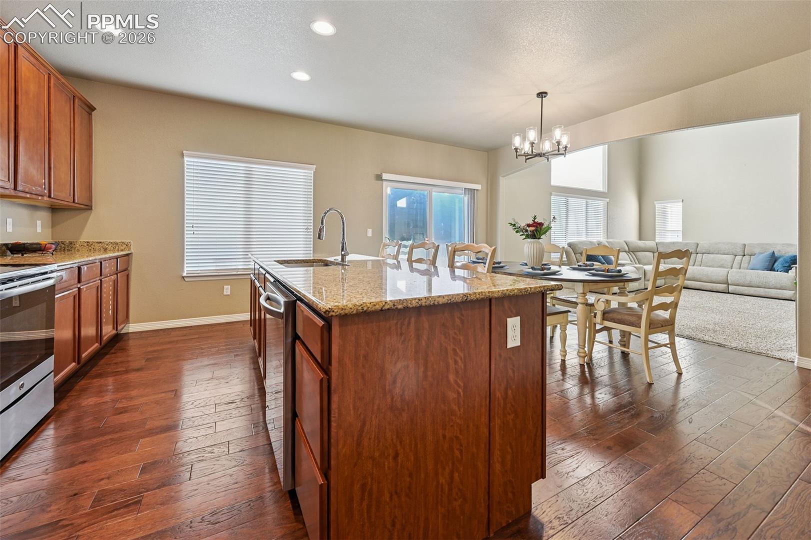 Kitchen with wood finish cabinets, light stone counters, dark wood-style flooring, a center island with sink, and stainless steel appliances