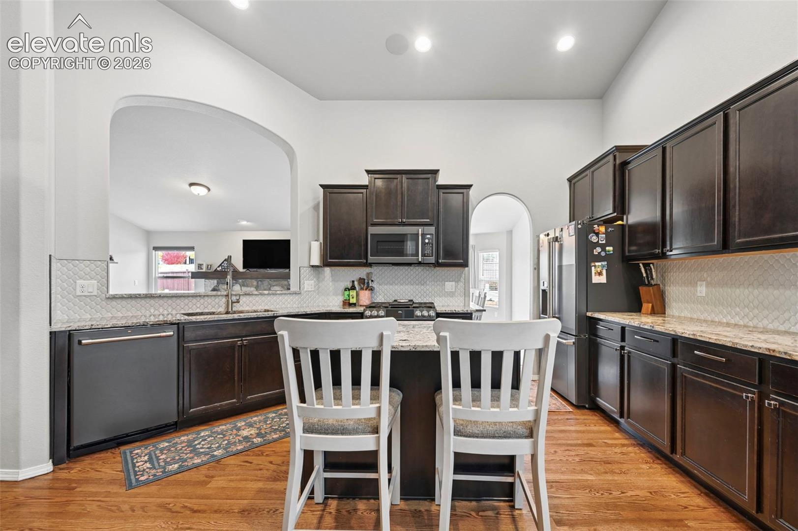 Kitchen featuring dark wood cabinetry, granite countertops, diamond-pattern backsplash, central island, and wood-finish flooring