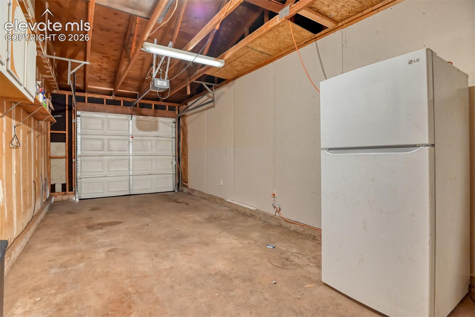 Attached garage space featuring an overhead door, exposed wooden ceiling joists, and concrete flooring