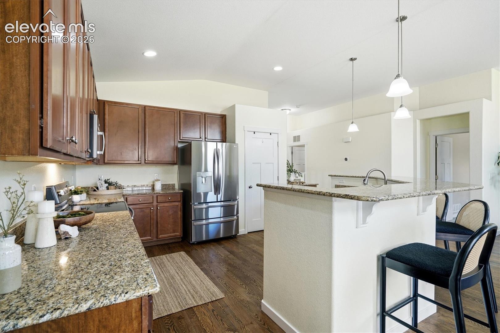 Kitchen featuring granite countertops, stainless steel appliances, wood-finish flooring, dark wood cabinetry, and pendant lighting