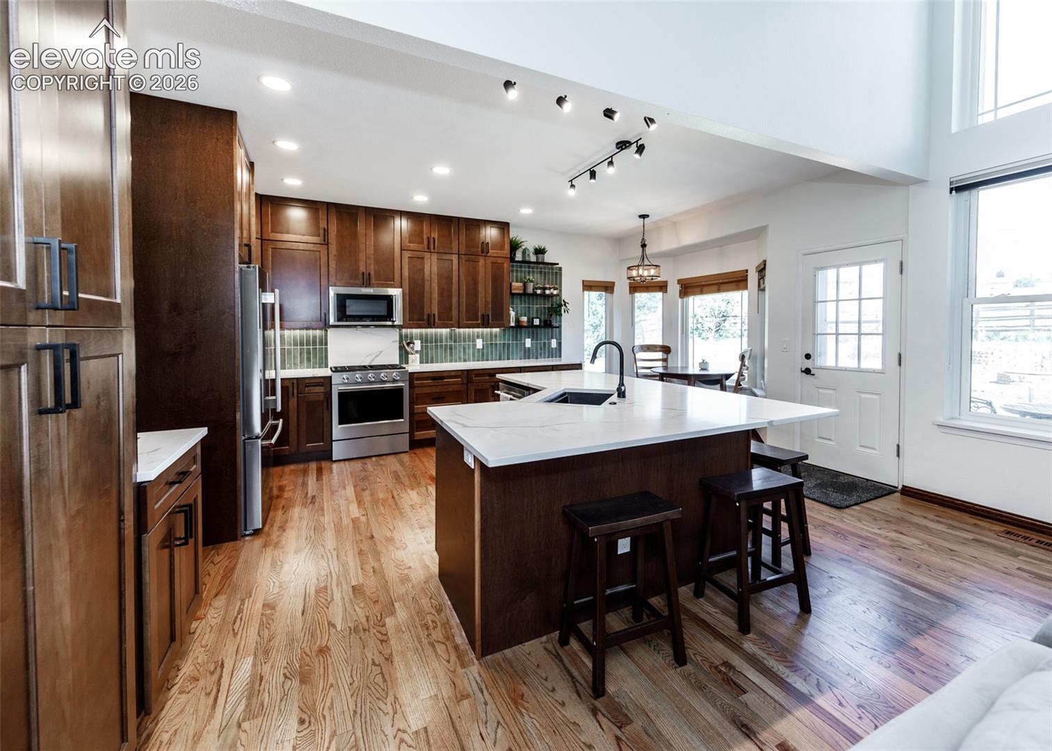Expansive kitchen featuring wood-finish flooring, dark wood cabinetry, a large kitchen island with white countertop, and stainless steel appliances
