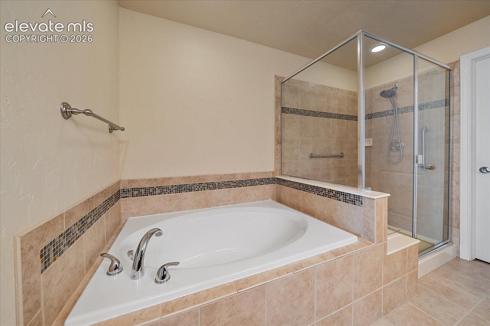 Corner soaking tub with a chrome deck-mounted faucet, glass-enclosed walk-in shower, and tile surround featuring decorative mosaic accent tiling