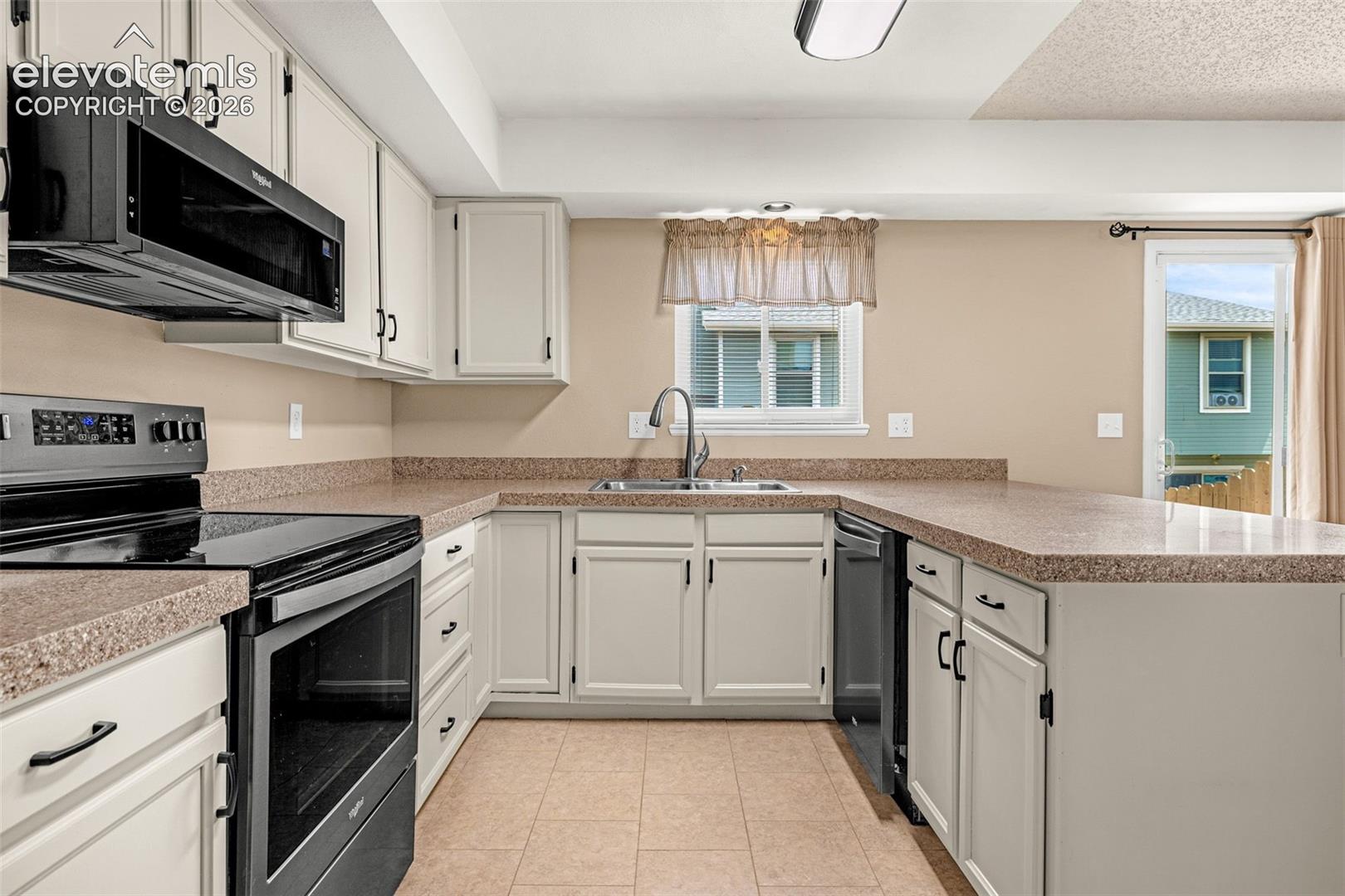 Kitchen featuring white cabinetry, dark-finish appliances, light-toned countertops, and tile flooring