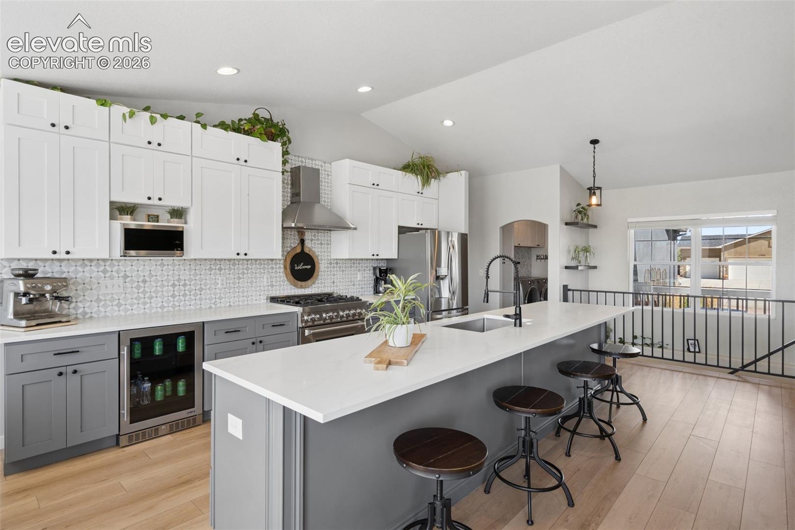 Gourmet kitchen with two-tone cabinetry, Pantry in island and laundry room professional-grade range, built-in beverage refrigerator, and quartz countertops