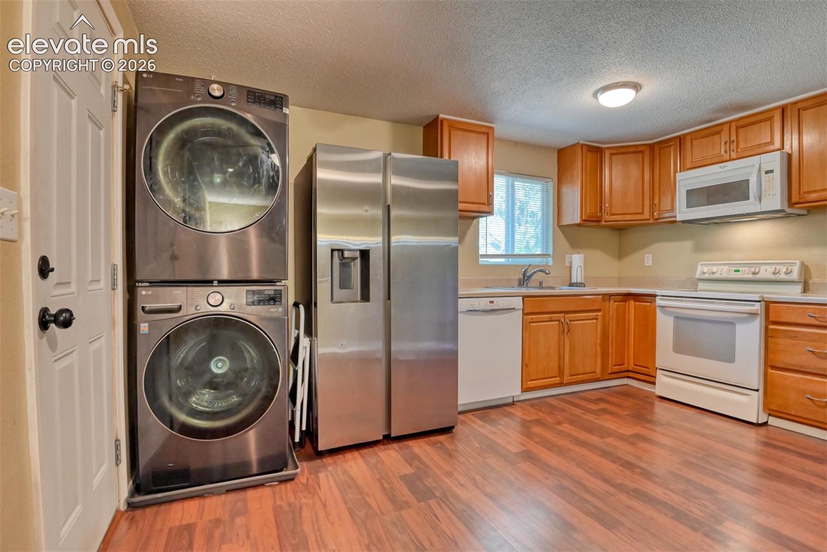 Kitchen featuring wood-finish flooring, wood cabinetry, stainless steel refrigerator, white dishwasher, and white range with an overhead microwave
