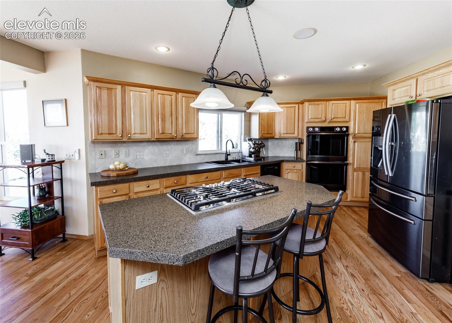 Kitchen featuring wood-finish flooring, natural wood cabinetry, a center island with a gas range, a built-in double oven, and a black French door refrigerator