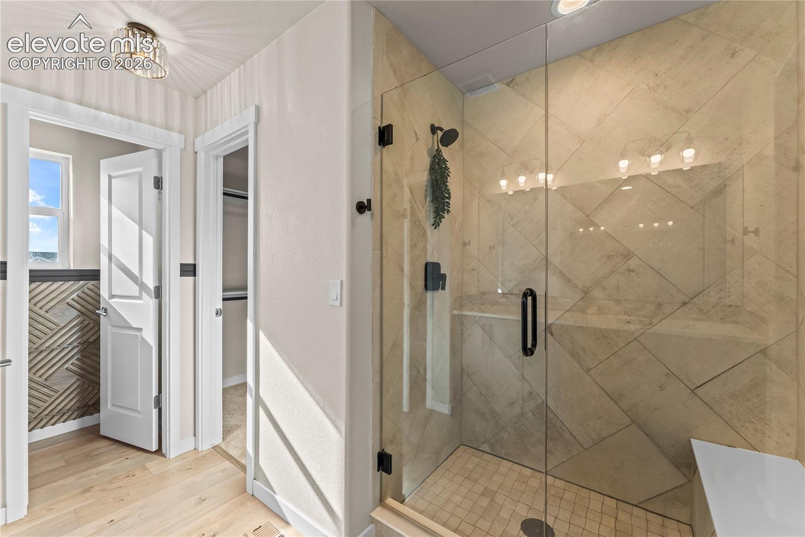Walk-in shower featuring glass enclosure, large-format tile surround in a diagonal pattern, mosaic tile floor, and matte black fixtures