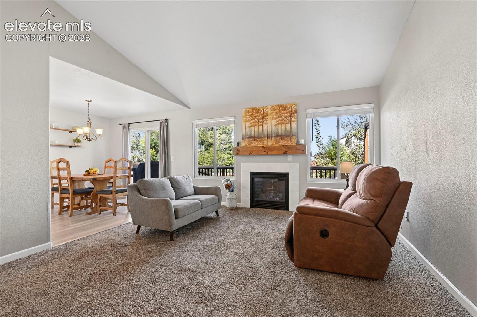 Vaulted ceilings, fireplace with natural stone surround, custom wood mantel, and large picture windows