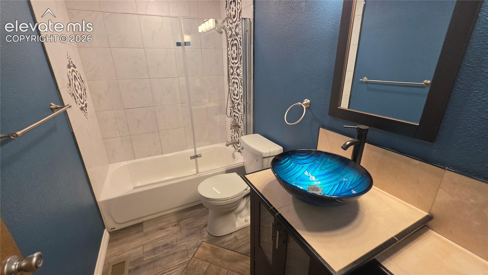 Bathroom featuring a vessel sink, vanity with storage, tile flooring, and a bathtub with a glass shower screen