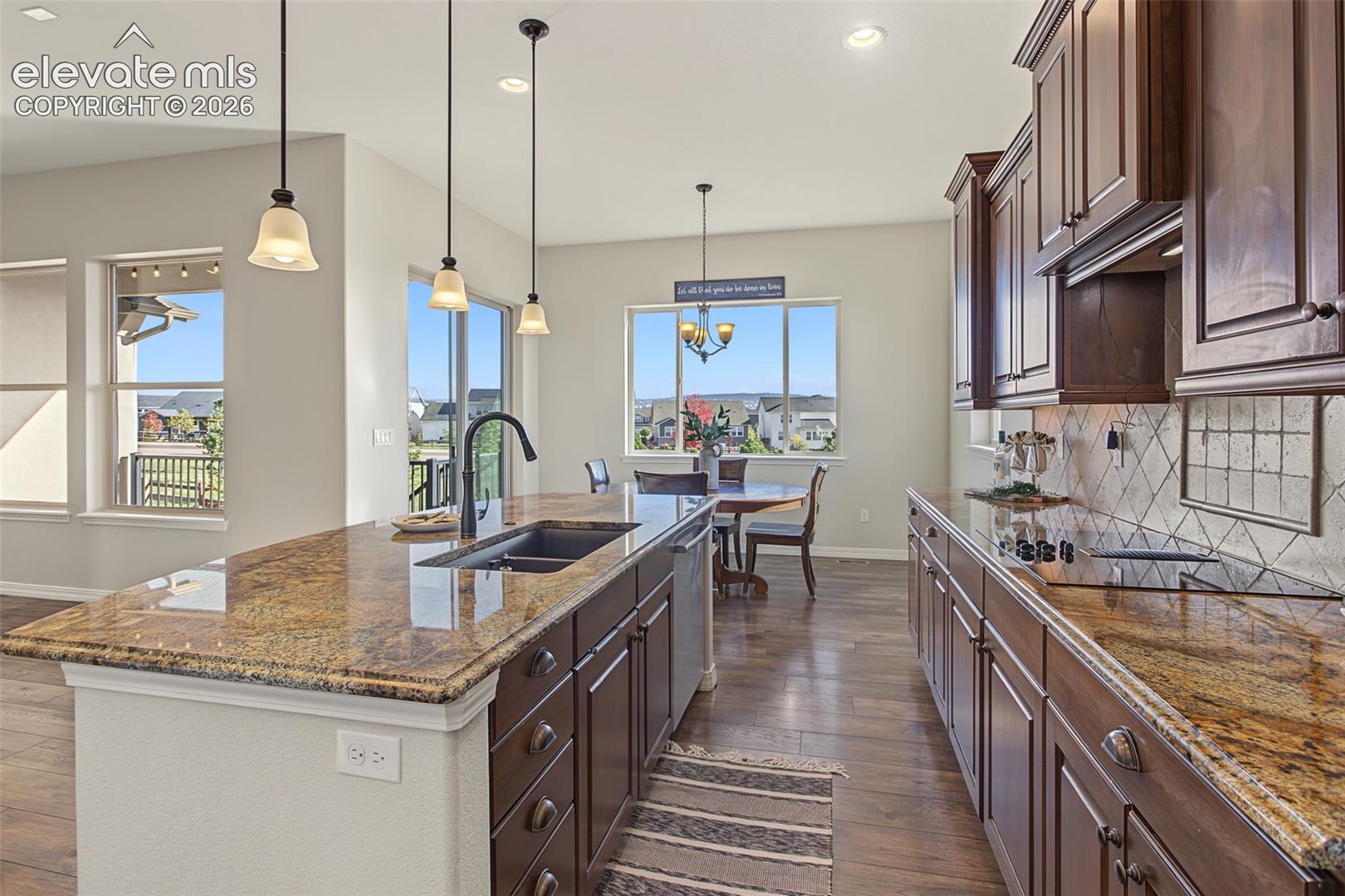 Kitchen featuring dark wood cabinetry, stone-surface countertops, center island with an undermount sink, pendant lighting, and wood-finish flooring