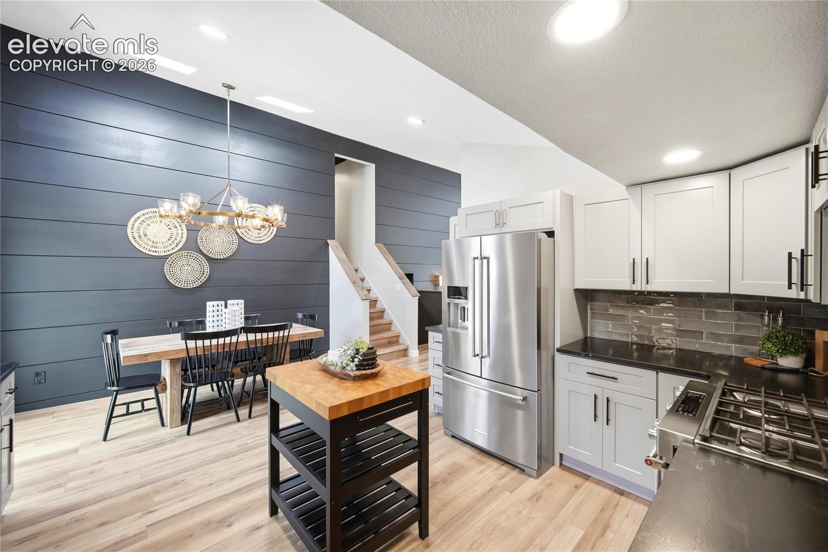 Kitchen and dining area featuring horizontal plank accent walls, wood-finish flooring, two-tone cabinetry, stainless steel appliances, and recessed lighting