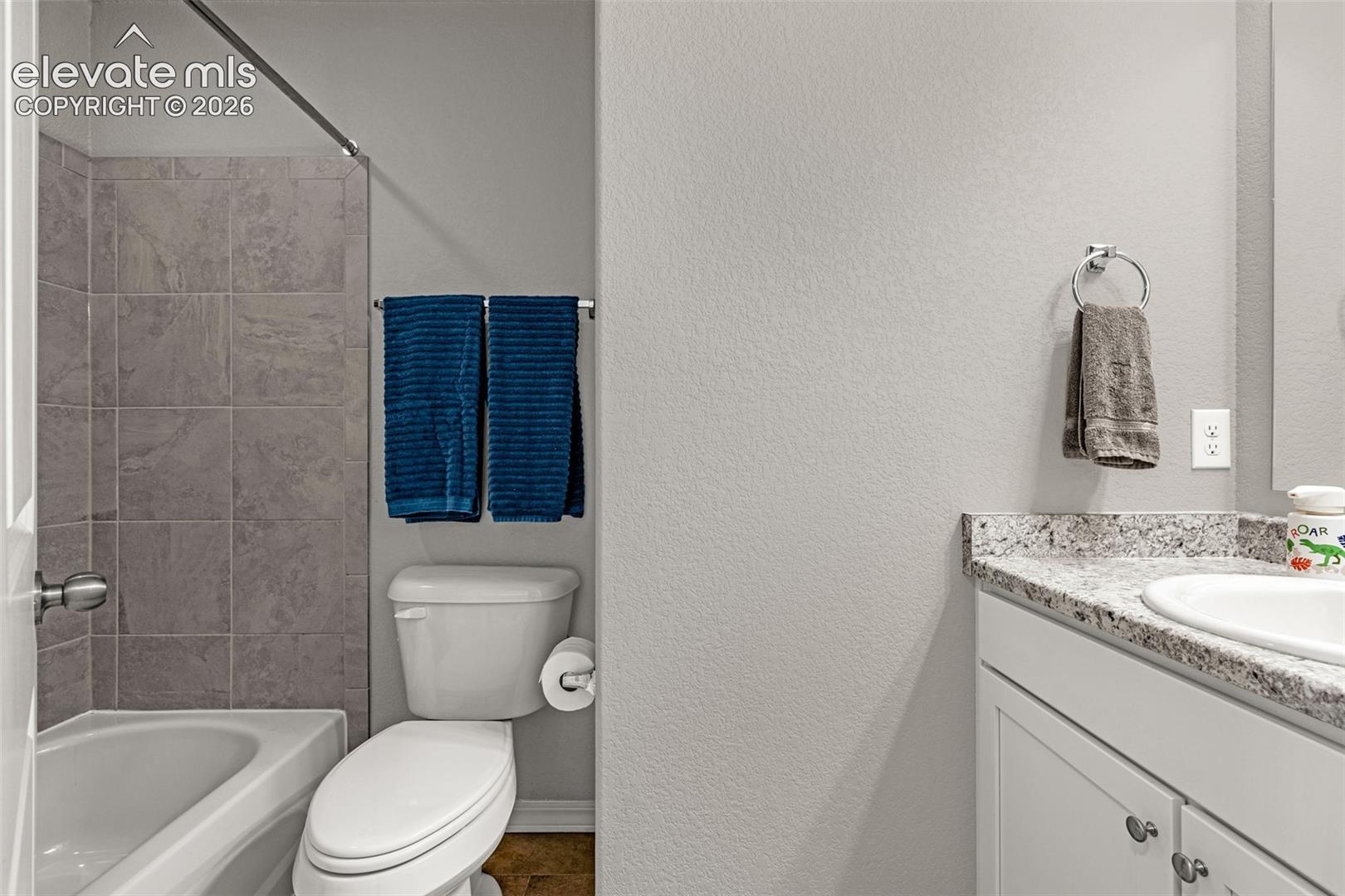 Bathroom featuring a white bathtub with a tiled shower surround, a white toilet, and a vanity with a light-colored countertop and undermount sink