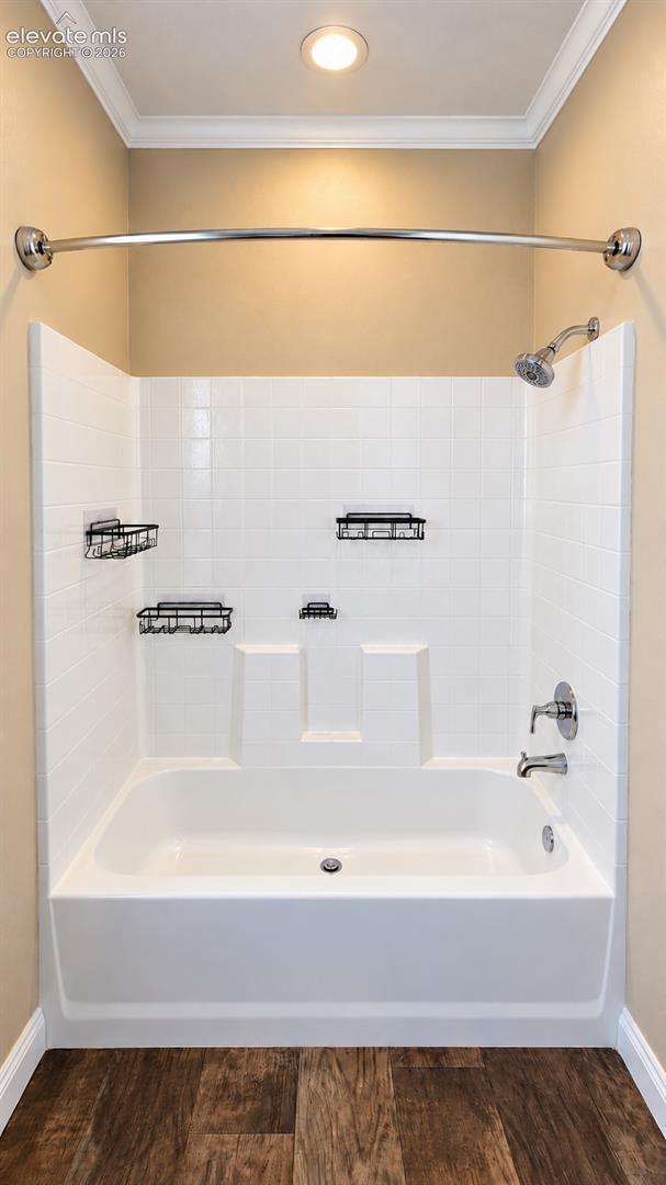 Bathtub and shower combination featuring white tiled wall surrounds, curved stainless steel shower rod, single-handle chrome plumbing fixtures, and wood-finish flooring
