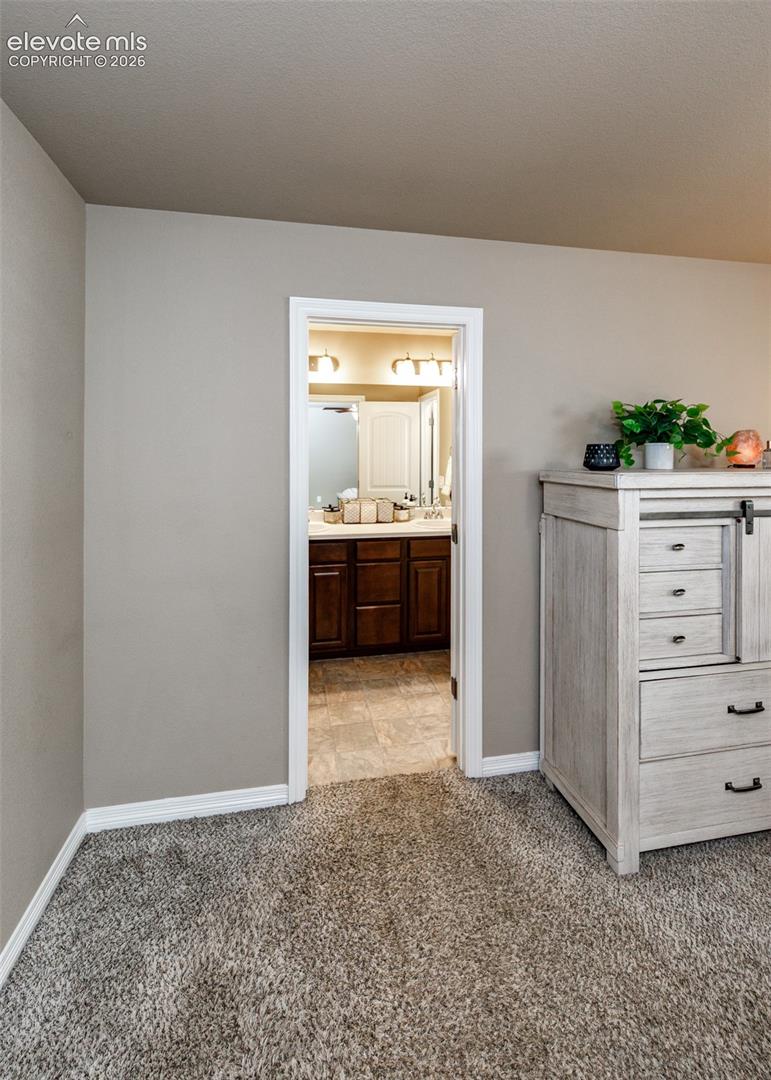 Neutral-toned interior featuring wall-to-wall carpeting and a bathroom entrance with dark-finish cabinetry, tile flooring, and multi-bulb vanity lighting