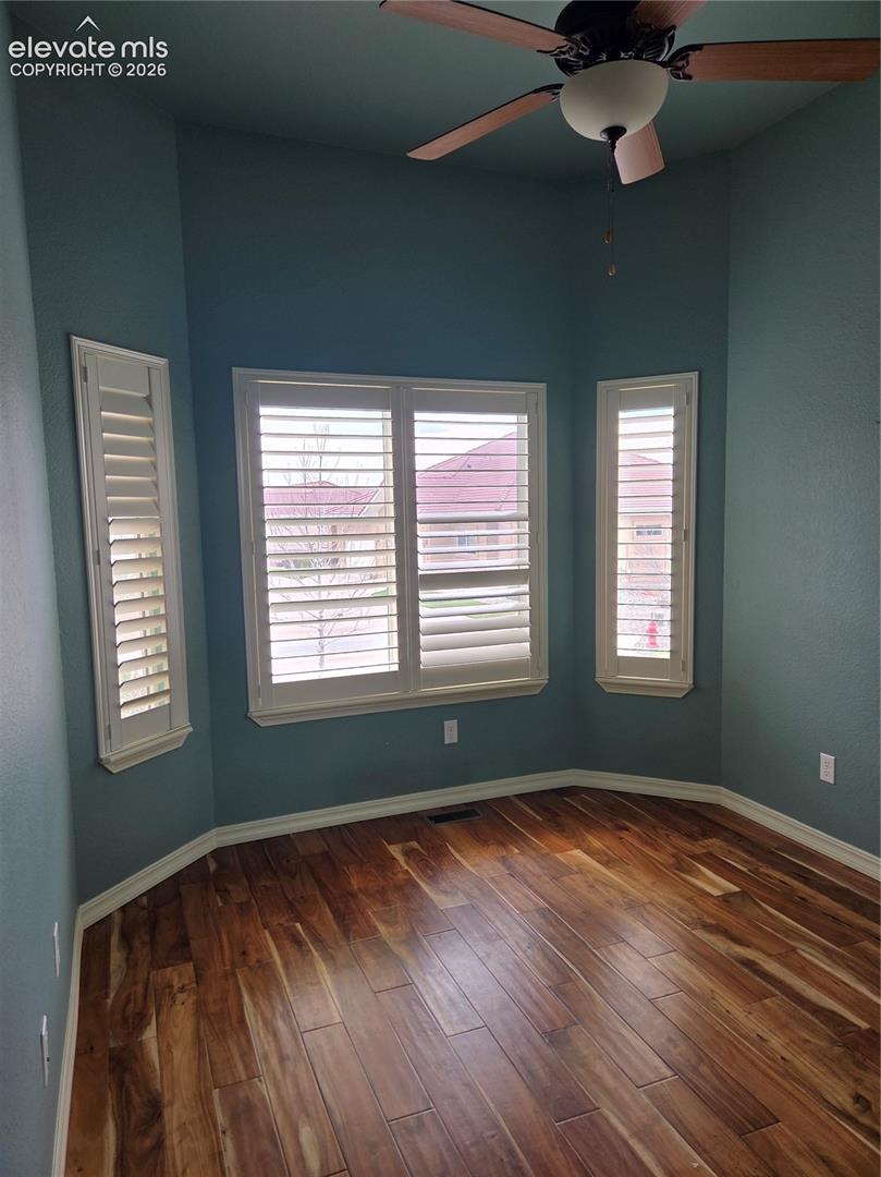 Bay window with plantation shutters, wood-finish flooring, ceiling fan with integrated lighting, and crown molding