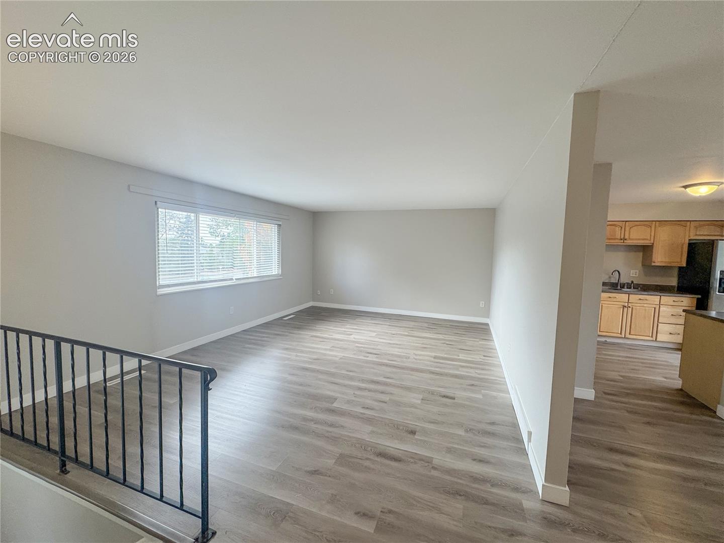 Open-concept interior featuring wood-finish flooring, a large picture window, and metal railing