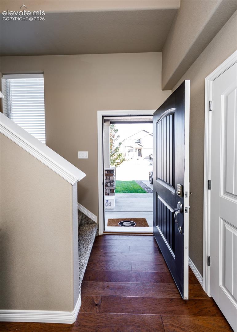Entryway featuring a dark-finished front door with a vertical glass panel, wood-finish flooring, and a staircase with neutral carpeted treads