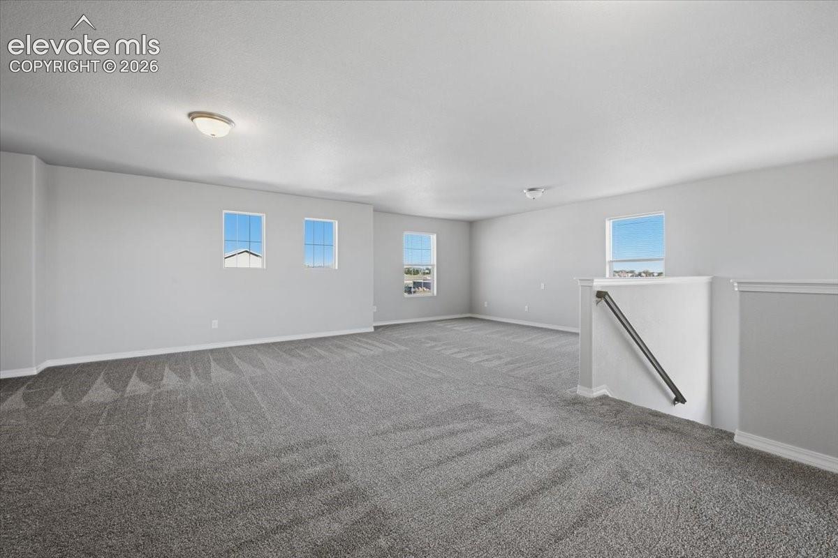 Expansive carpeted area featuring neutral wall paint, multiple windows with grid detailing, recessed lighting, and a metal handrail