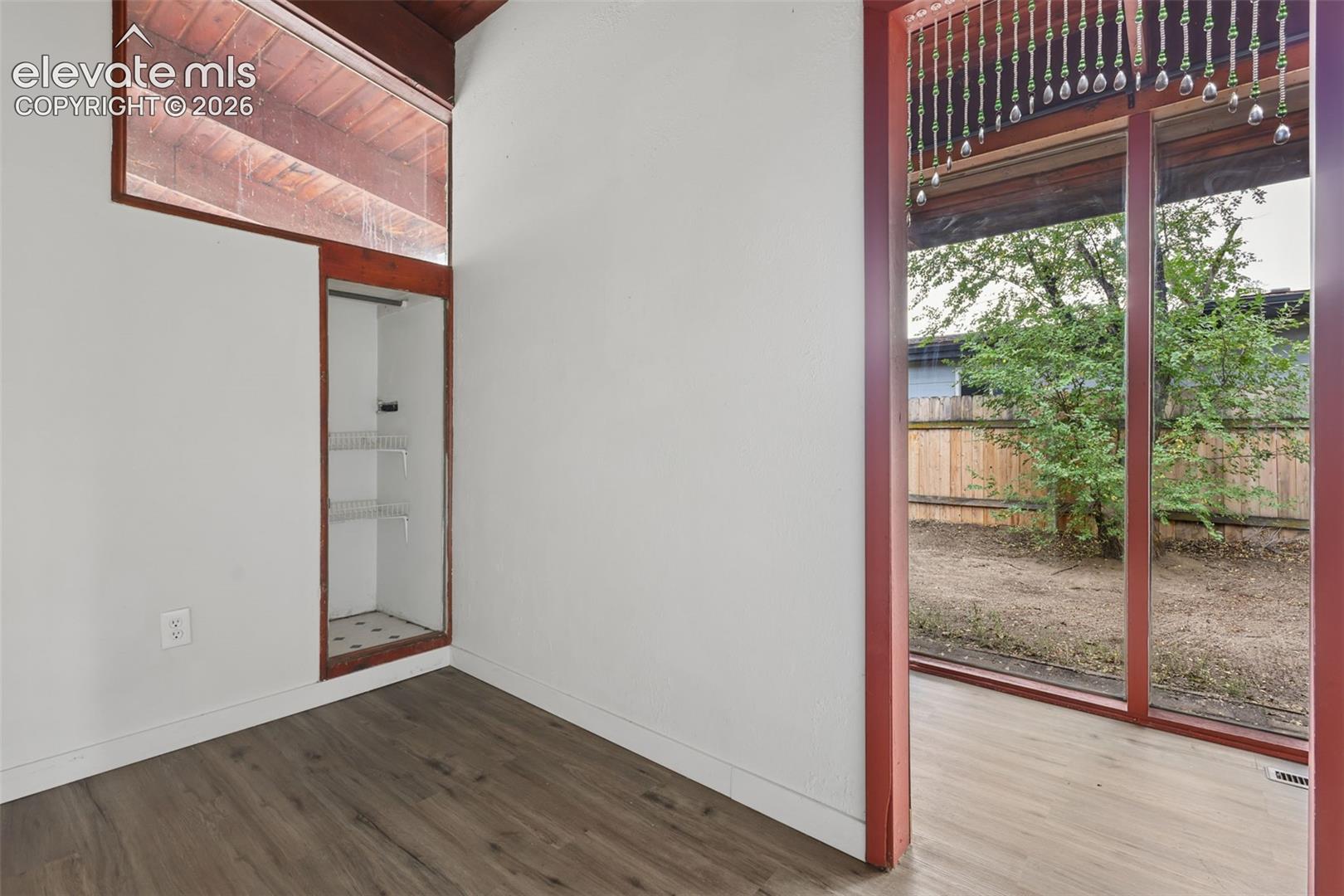 Expansive full-height window, wood-finish flooring, built-in shelving, vaulted wood-paneled ceiling, and a private fenced yard