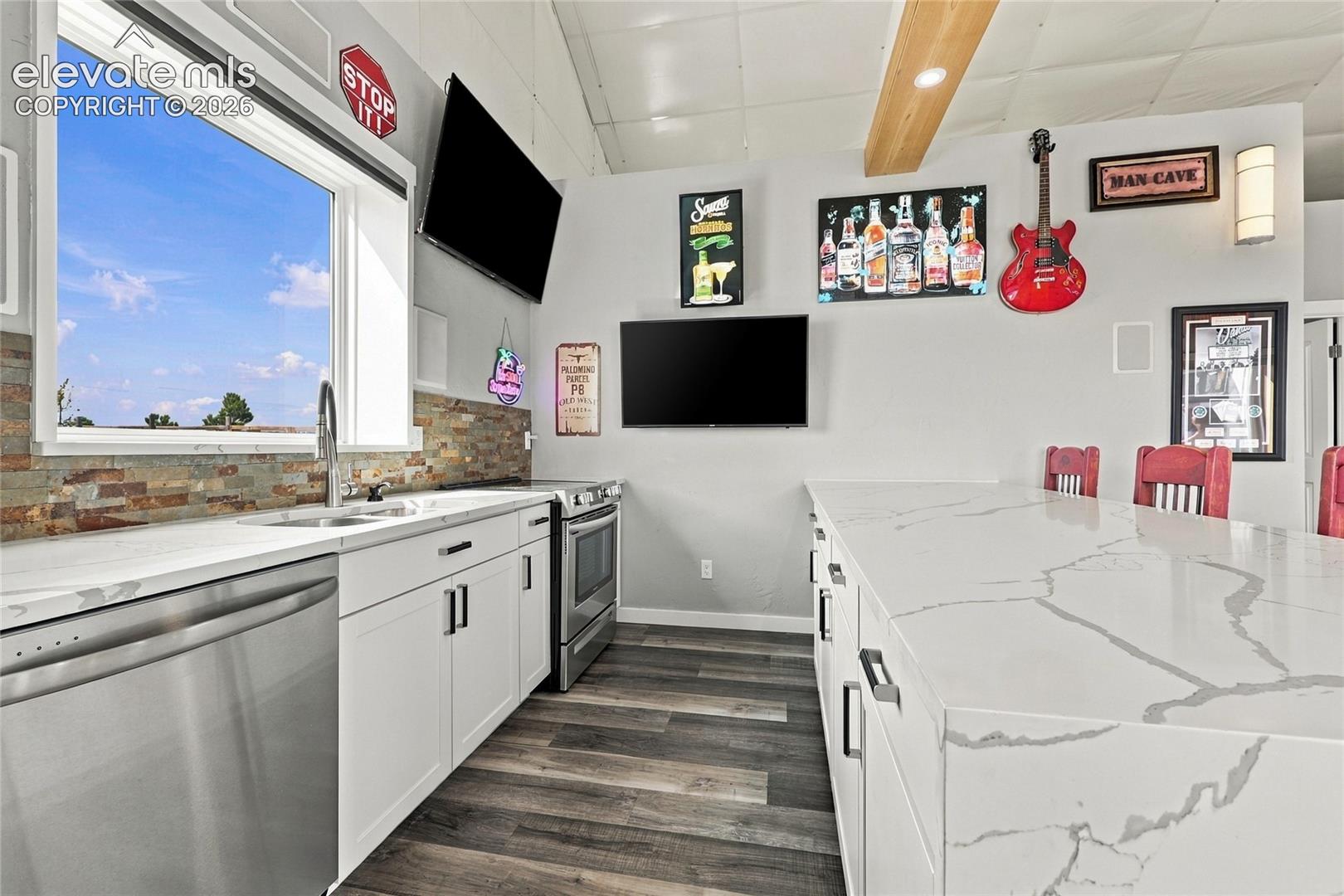 Kitchen featuring a large waterfall-edge island with solid-surface countertops, wood-finish flooring, stacked stone backsplash, and stainless-steel appliances
