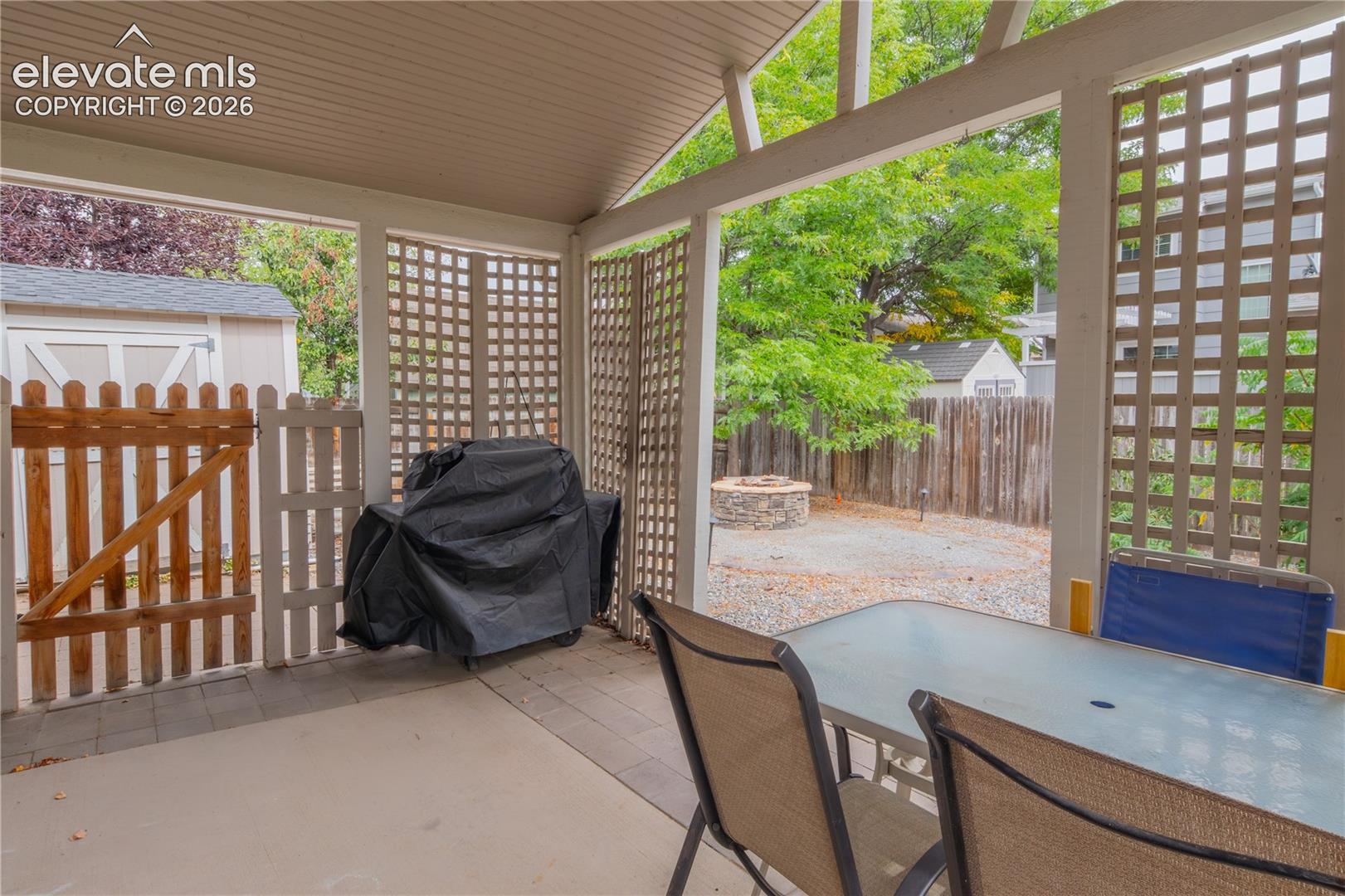 Covered patio with concrete flooring, lattice privacy screens, and a wood picket fence