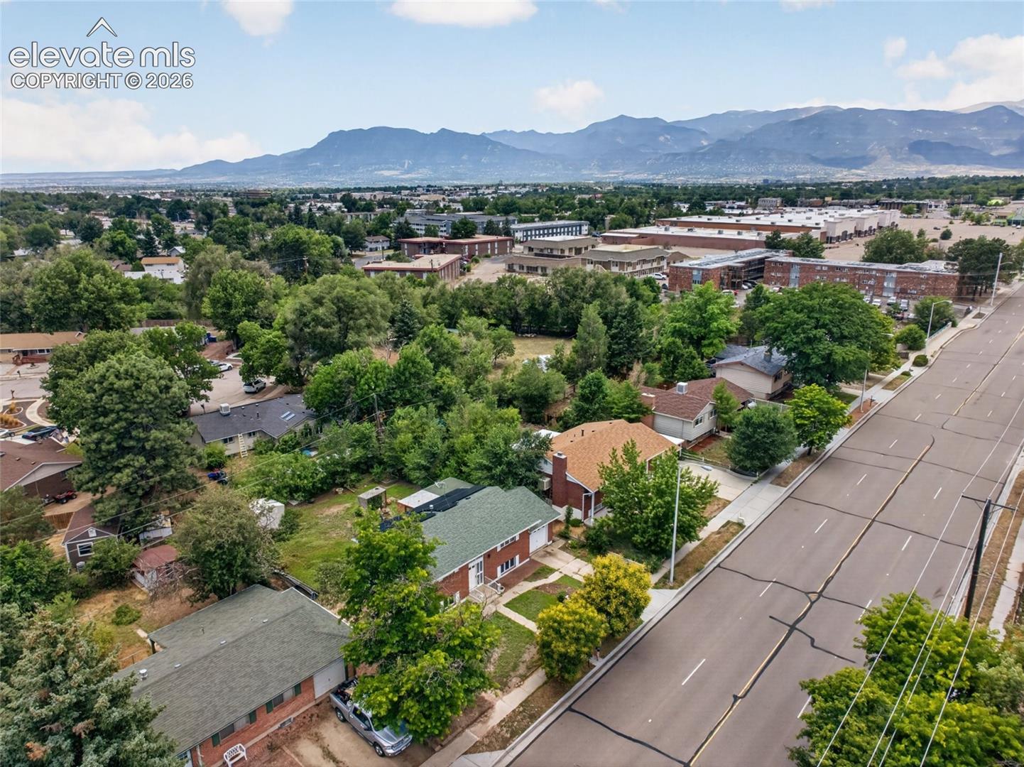 Aerial perspective featuring residential structures with shingled roofing, mature landscaping, and a prominent mountain range backdrop