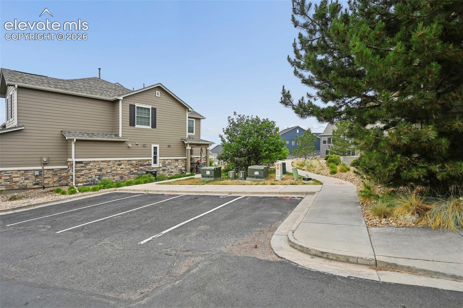 Exterior featuring tan horizontal siding, stone veneer accents, dark shutters, and an asphalt parking area with designated spaces