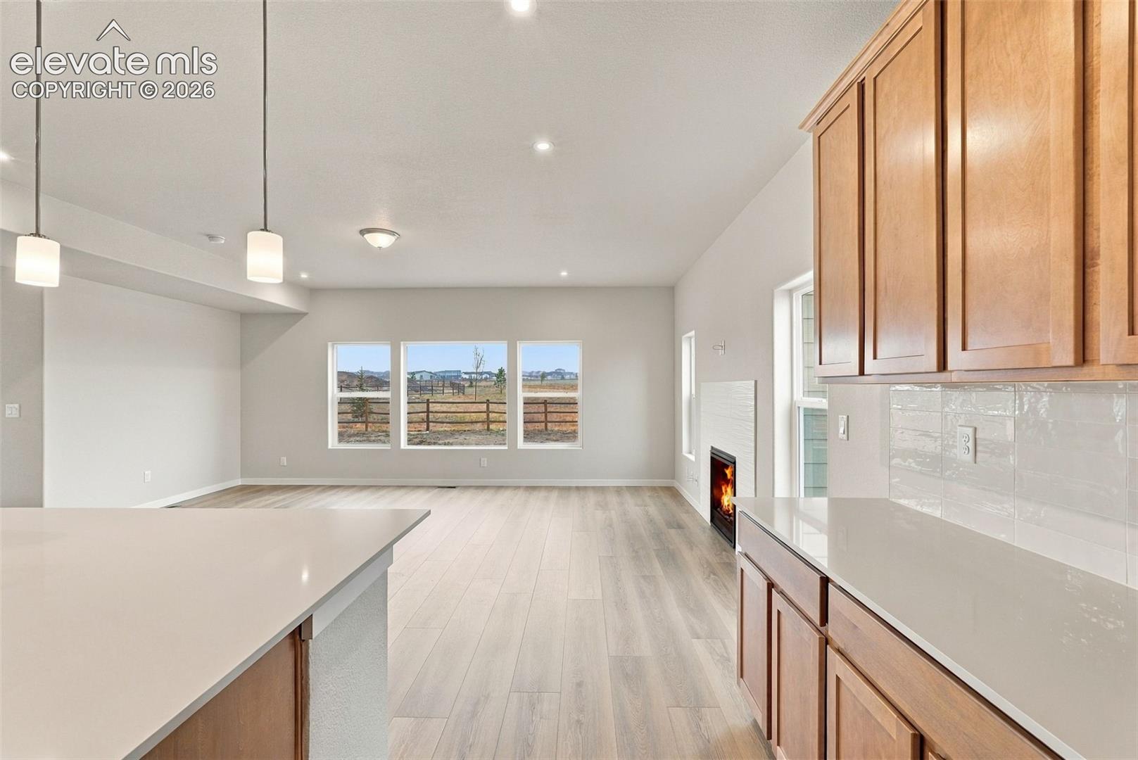 Kitchen featuring wood cabinetry, quartz countertops, white tile backsplash, pendant lighting, and wood-finish flooring