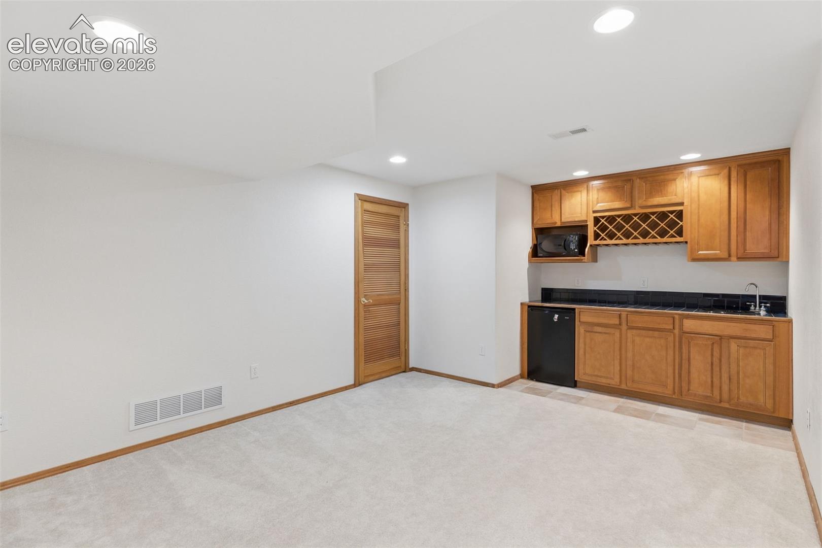 Built-in wet bar featuring custom wood cabinetry, integrated wine storage, a dark solid-surface countertop, and a stainless steel sink