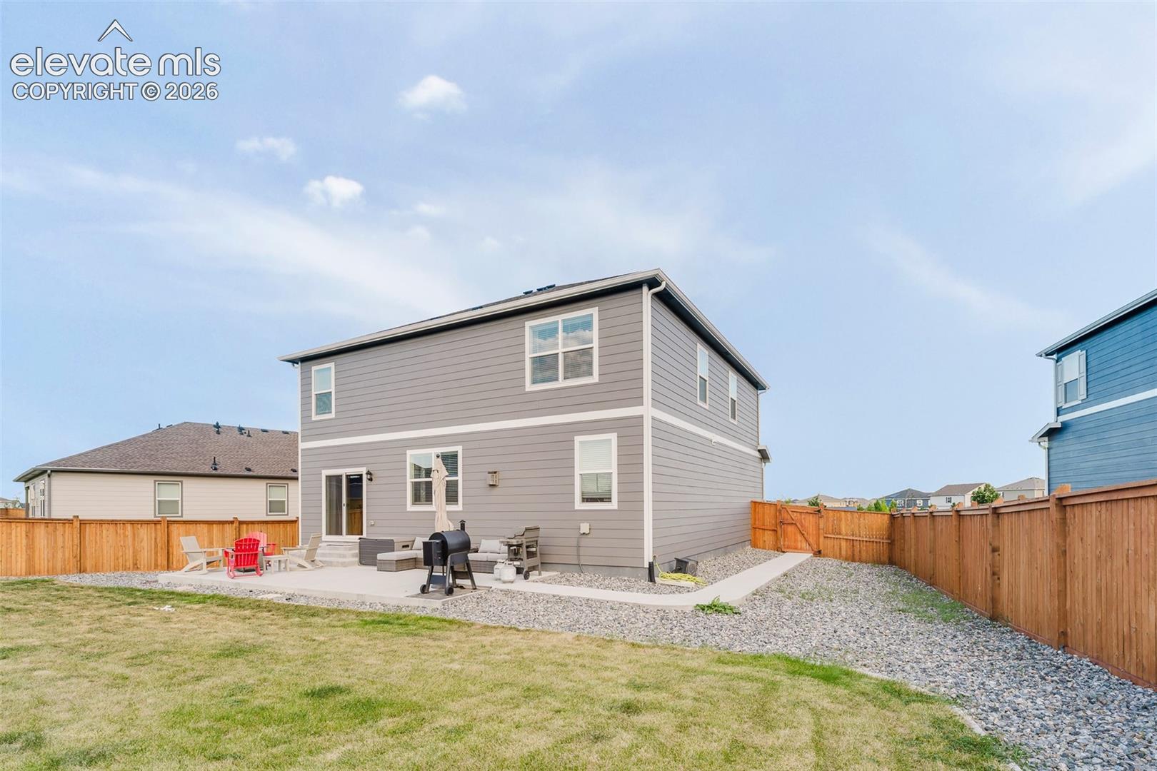 Rear view of fenced backyard, concrete patio, and side yard walkway to the front of the house.