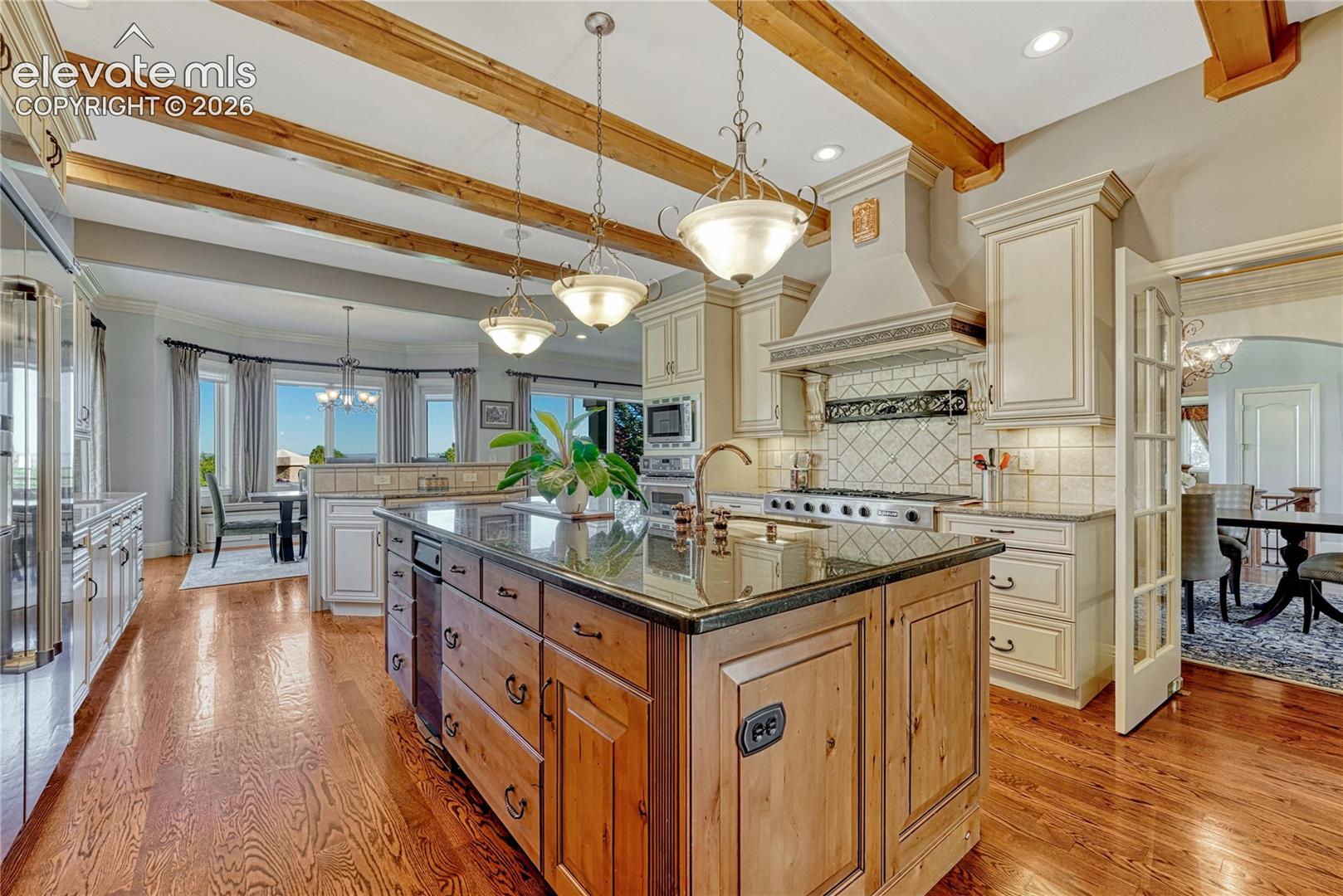 Kitchen featuring wood-finish flooring, exposed ceiling beams, a center island with countertop seating, custom cabinetry, and stainless-steel appliances
