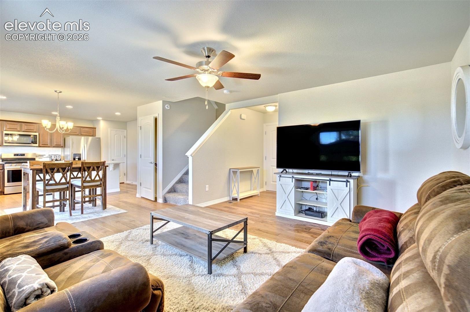 Open-concept main level featuring wood-finish flooring, ceiling fan with integrated lighting, kitchen with wood cabinetry, and a carpeted staircase