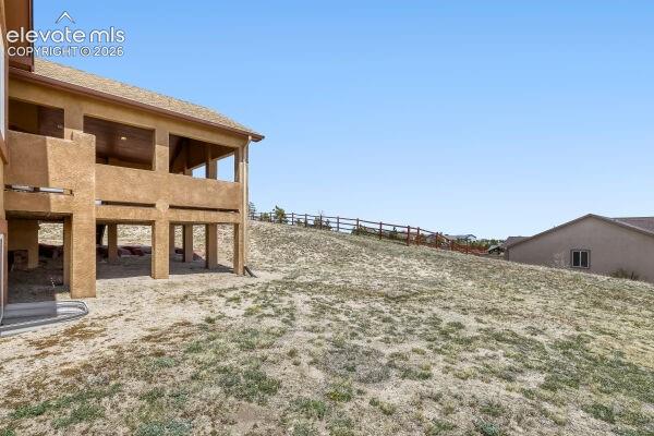 Expansive sloped property featuring a covered patio, a covered balcony, and a visible wood fence line