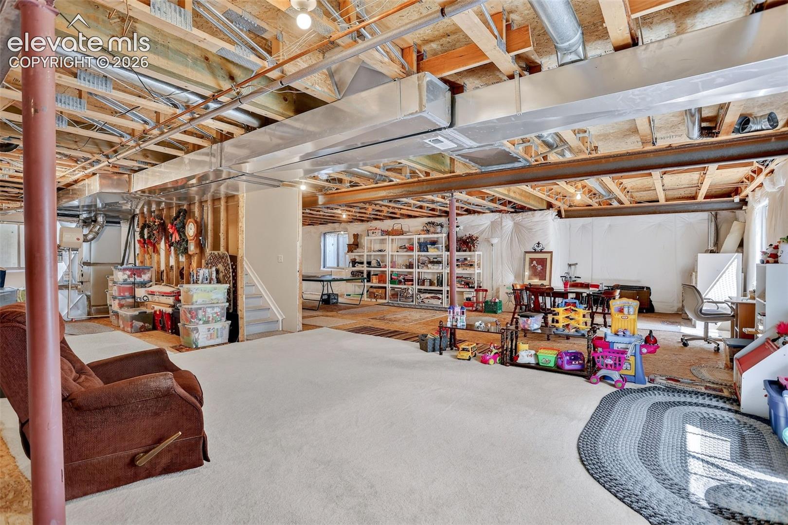Unfinished lower level featuring exposed ceiling joists and ductwork, a carpeted area, and a staircase