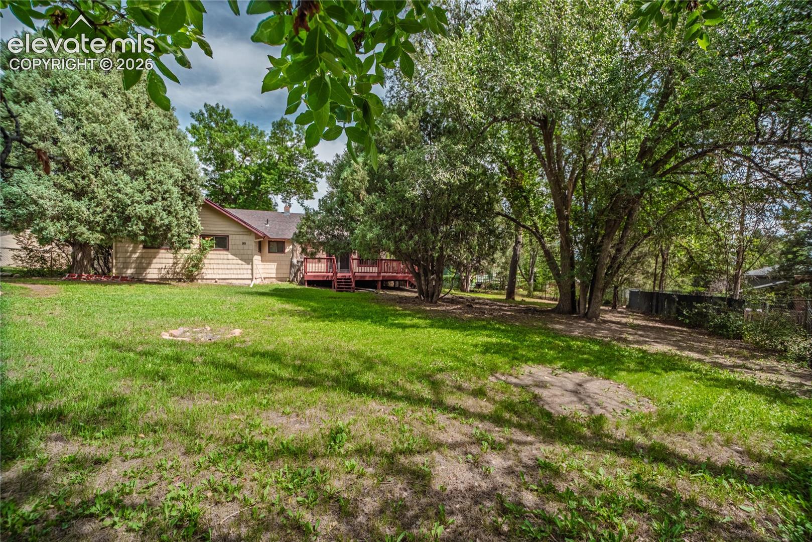 Expansive backyard with a manicured lawn, mature trees, and a multi-level wood deck