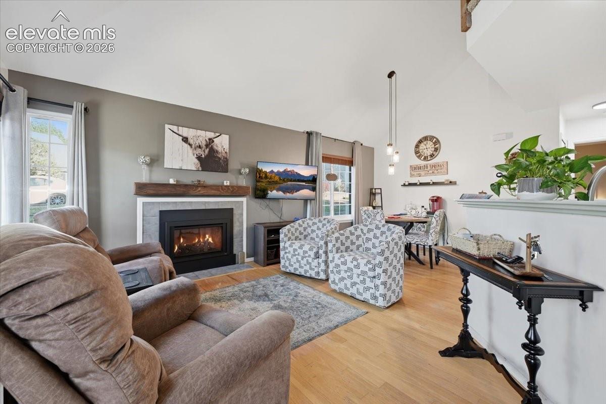 Vaulted ceilings, wood-finish flooring, fireplace with stone surround and wooden mantel, and multi-pendant lighting