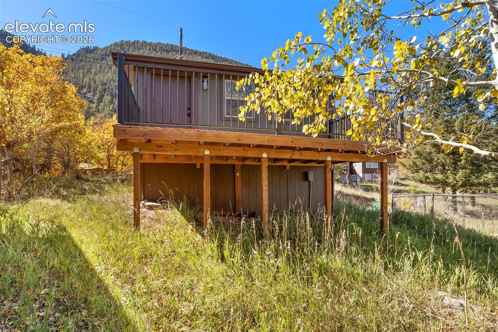 Exterior featuring vertical wood-paneled siding, an elevated wooden deck with black metal railing, and a mountainous backdrop