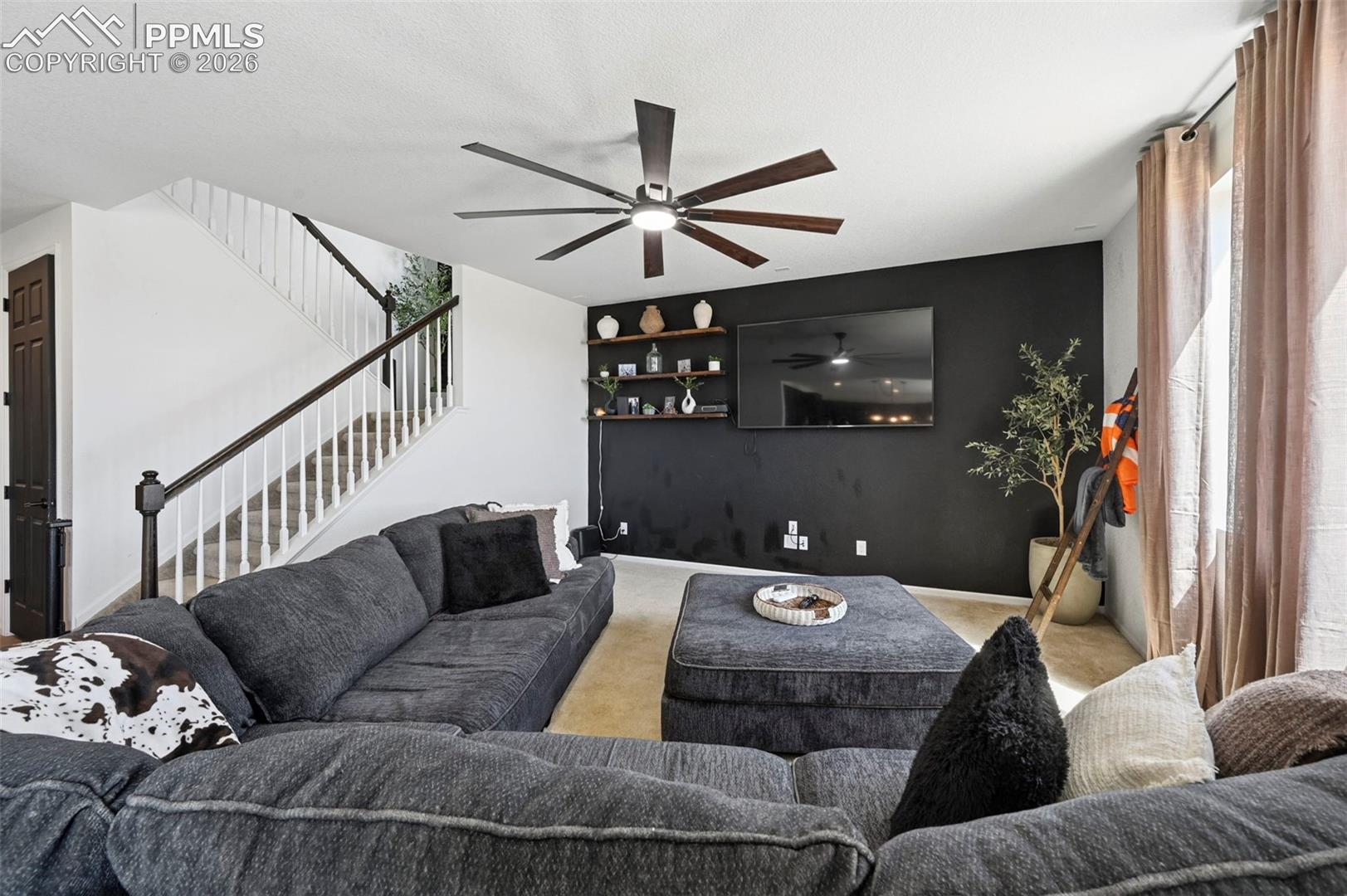 Bright living area featuring a modern ceiling fan with wood-finish blades, a striking black accent wall, and built-in shelving