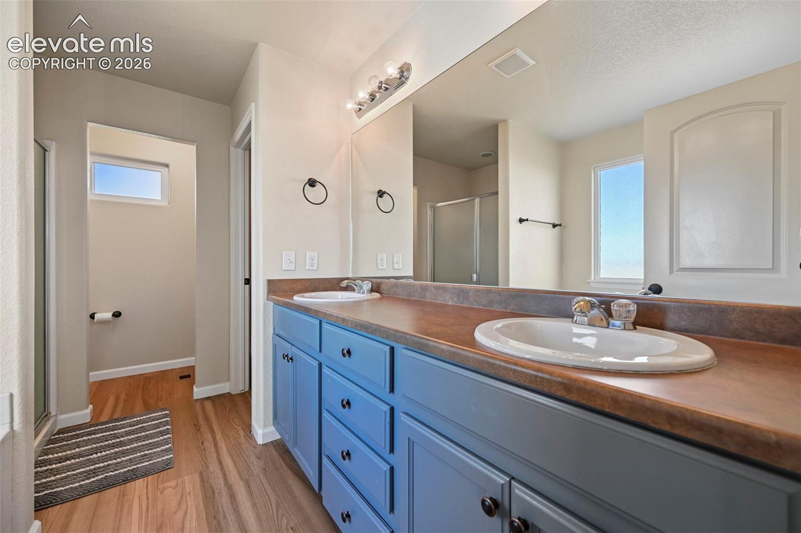 Double vanity featuring dual drop-in sinks, a full-width mirror, light-toned wood-finish flooring, and painted cabinetry