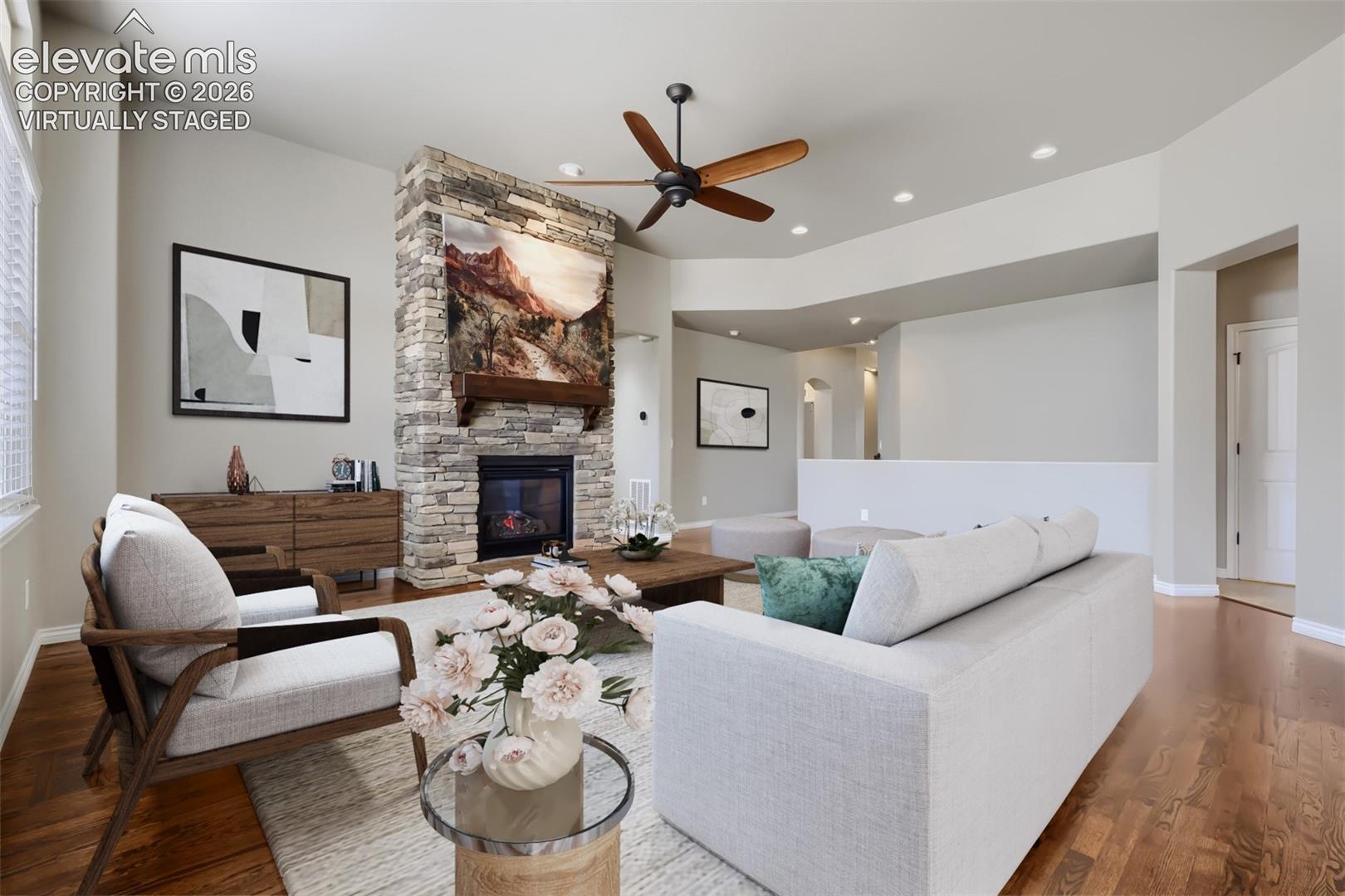 Virtually staged living room with picture windows, stone fireplace, open concept design, gorgeous wood floors.