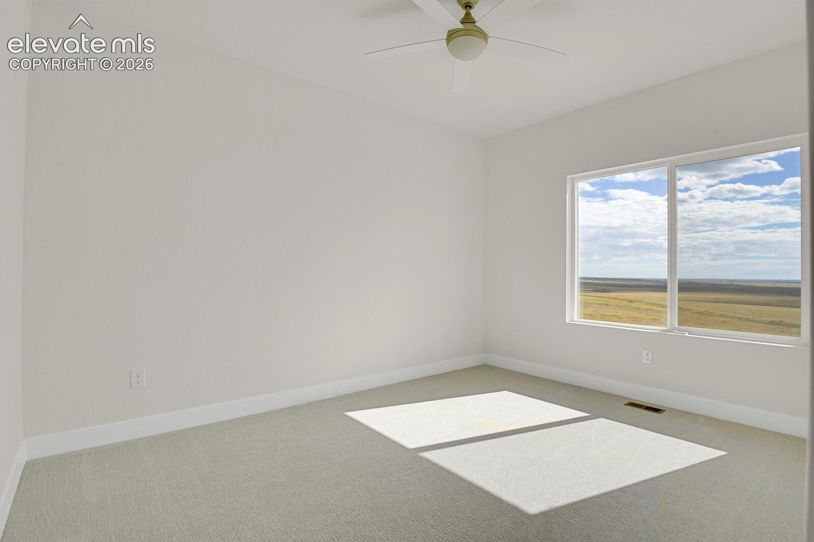 Neutral-toned carpeting, white walls, ceiling fan with integrated lighting, and large picture window showcasing expansive terrain