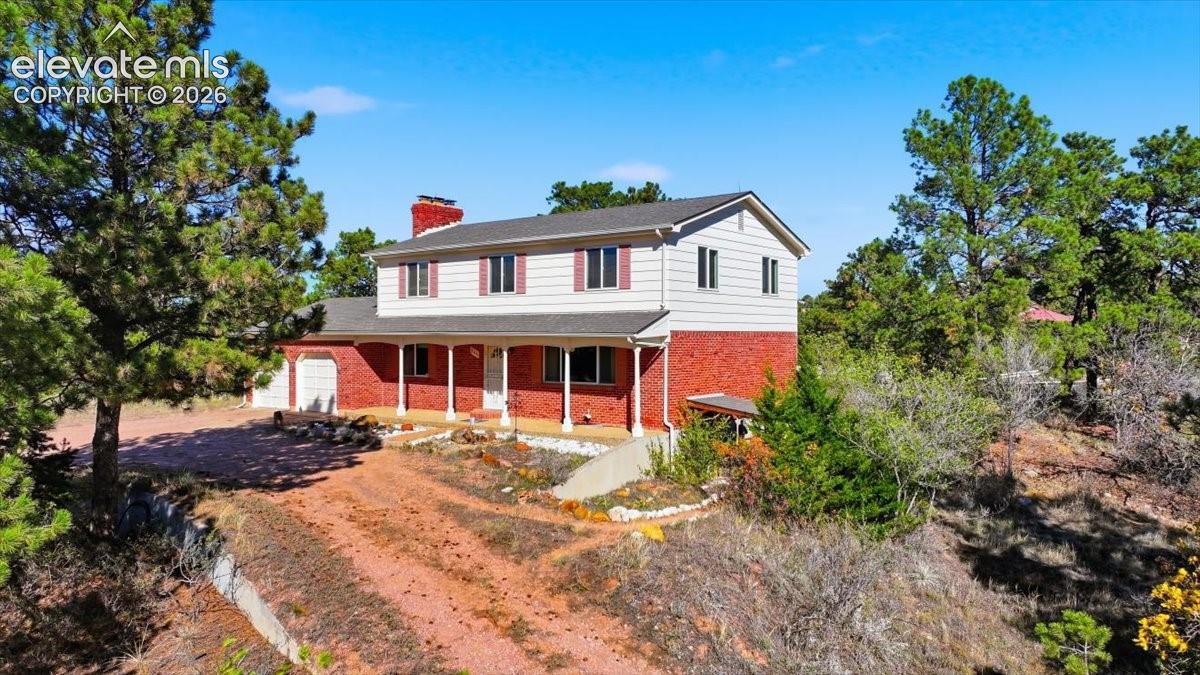 Two-story residence featuring a classic red brick lower level, lap siding upper exterior, covered front porch with support columns, brick chimney, and an attached garage