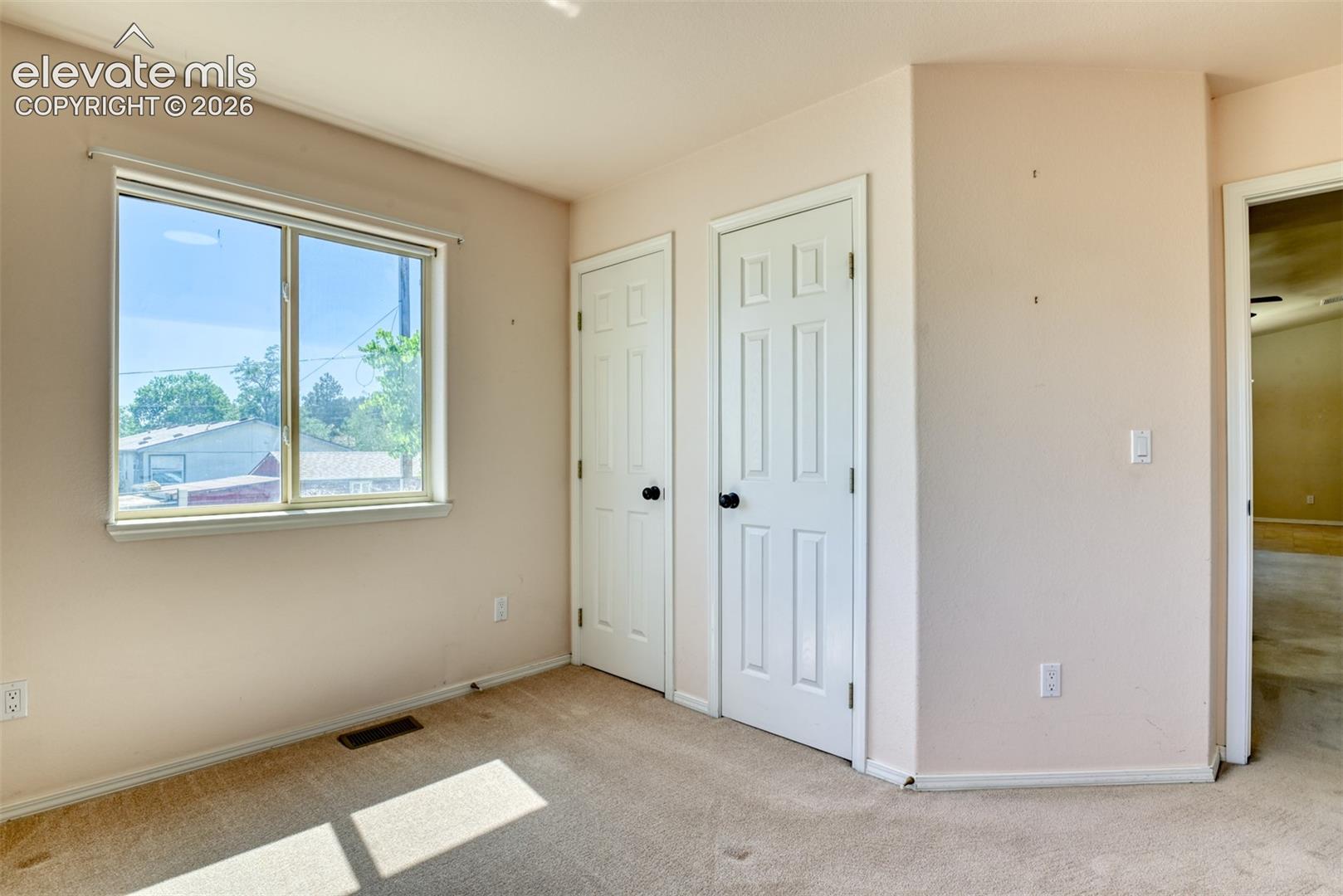 Room featuring neutral-toned carpeting, a horizontal sliding window, and two paneled interior doors with round matte black hardware