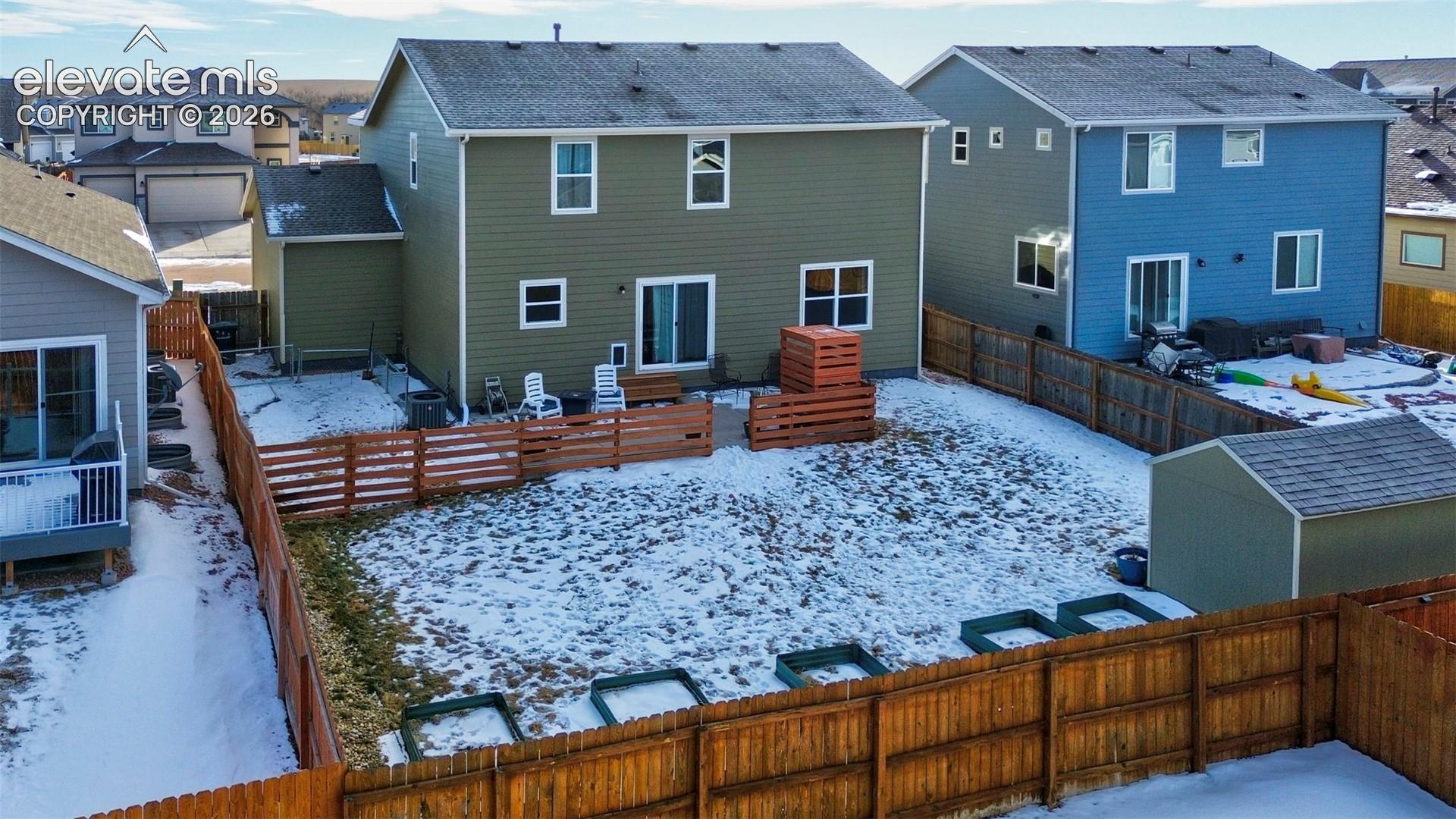 Rear exterior featuring horizontal lap siding, a fenced backyard, raised garden beds, and a detached storage shed