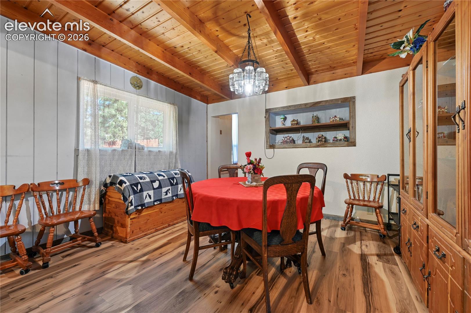 Wood-finish flooring, exposed wood beam ceiling, recessed wall shelving, and a prominent window