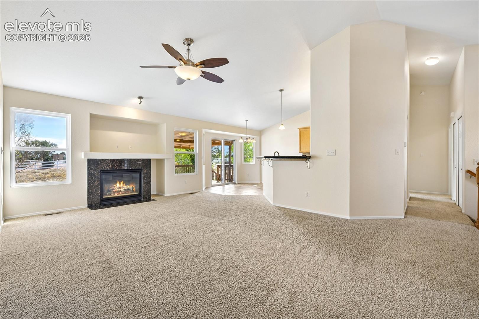 Vaulted ceilings, a built-in fireplace with a stone surround, and an integrated ceiling fan