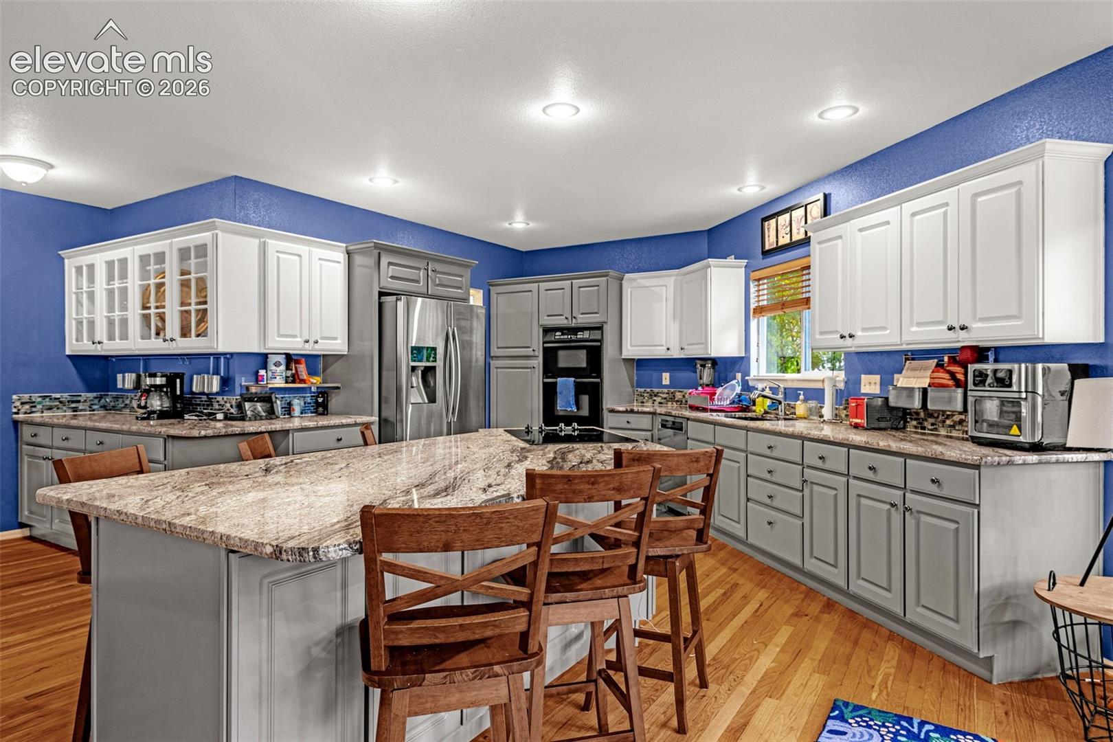 Kitchen featuring a large island with stone countertop, stainless steel appliances, recessed lighting, wood-finish flooring, and ample cabinetry