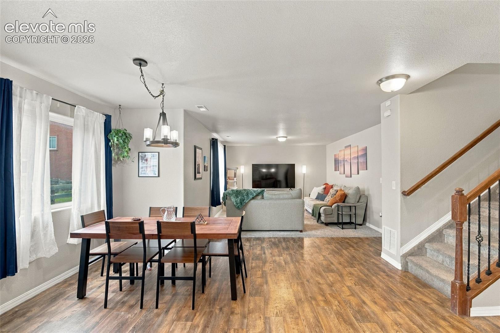Open-concept interior featuring wood-finish flooring, a multi-light chandelier, recessed ceiling lighting, and a staircase with a wooden handrail and metal balusters