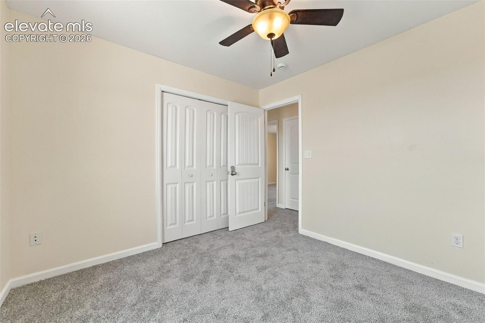 Neutral wall finishes, carpeted flooring, built-in closet with paneled doors, and a ceiling-mounted light fixture with fan